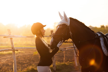 Fototapeta na wymiar beautiful girl stands with a horse in the rays of a setting sun