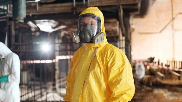 Caucasian young man wearing yellow hazmat suit looking attentively at camera. Portrait of Slavic ecologist in gas mask. Indoors.