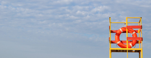 Orange lifeline on yellow lifeguard tower on blue sky background. Banner