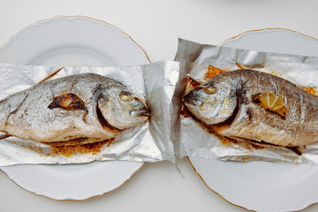 Two gilt-head bream fish on the aluminum foil on white table - view from above od delicious food...
