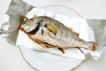 One gilt-head bream fish on the aluminum foil on white table - view from above od delicious food homemade