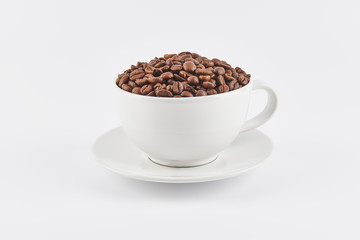White coffee cup filled with whole coffee beans on a saucer, isolated on white background.