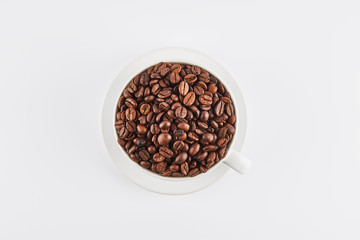 Flat lay of white coffee cup filled with whole coffee beans on a saucer, isolated on white background. Top view.