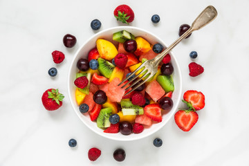 fruit salad with watermelon, strawberry, cherry, blueberry, kiwi, raspberry and peaches with fork in a bowl