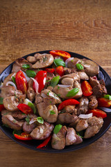 Chicken liver with  tomatoes, onions and basil on black plate, wooden table. vertical