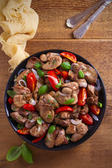 Chicken liver with  tomatoes, onions and basil on black plate, wooden table. overhead, vertical