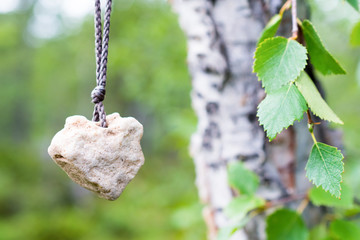 The heart of stone hanging on a rope on a birch