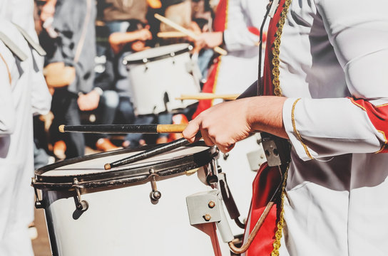 Member of a military fanfare playing a mobile bass drum. Playing a mobile bass drum with drumsticks. Bass drum attached to the body, musician walking and playing on a parade.