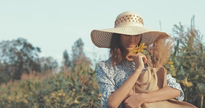 beautiful sweet sexy girl in a blue dress and hat walking on a field of sunflowers , cheerful woman sniffing flowers, countryside style, lifestyle 4K video shooting by handheld gimbal
