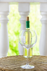 Empty glass bottle with white dry wine on wicker table on garden terrace of villa or mansion. Authentic lifestyle image. Relaxation indulgence gourmet. Poster with copy space