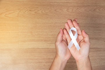 women hands holding white bow, white ribbons on wooden background. Awareness White ribbon for...
