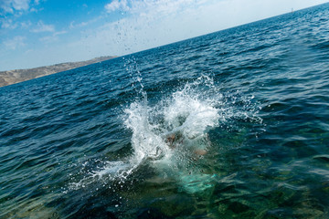 A boy is jumping from the cliff into the sea wiht big water splash on a hot summer day. Holidays on the beach. The concept of active tourism and recreation