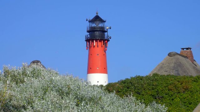 Leuchtturm H&ouml;rnum Sylt mit D&uuml;nen Landschaft  Reetdach H&auml;usern und  blauen Himmel
