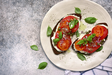 Rye toasts with soft cheese, tomato, red onion and capers.Top view with copy space.