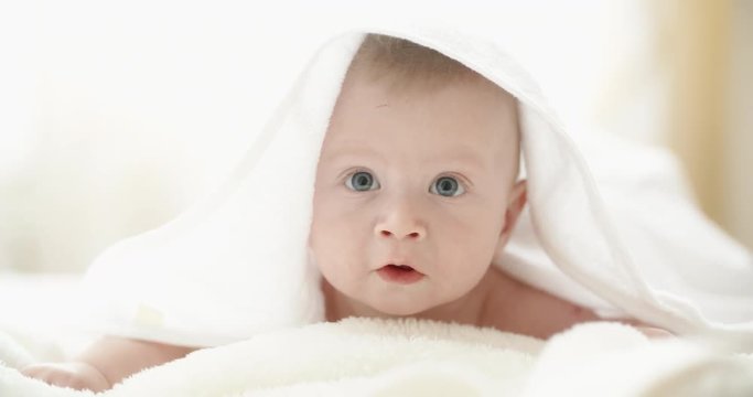 A cute happy baby lying on white bed sheet, looking around and happily laughing and smiling. closeup 4k