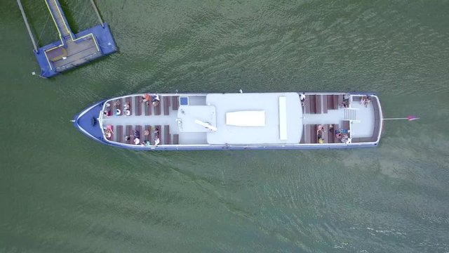 Following a Small tourist cruise boat as it is approaching a small dock, with people on the upper deck at lake Lipno, South Bohemia - Top down aerial footage.