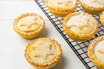 Homemade mince pies. Traditional British Christmas pastry dessert with apples raisins nuts filling on metal cooling rack. Golden Shortcrust Powdered. White Wood Table Copy Space