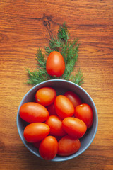Fototapeta na wymiar Fresh ripe cherry tomatoes in the blue bowl with fresh dill, overhead shot