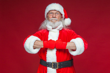 Christmas. Santa Claus with red bandages wound on his hands for boxing imitates kicks. Kickboxing, karate, boxing. Isolated on red background.