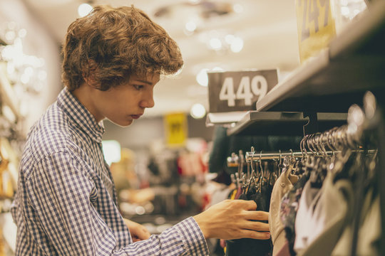 portrait of young teenager choosing and picking right clothes in store