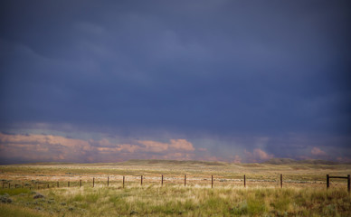 Fenced pasture land under a stormy blue sky in a afternoon summertime landscape in rural montana