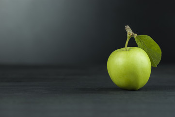 green fresh apple with leaf on black wooden table 