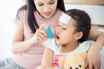 Obraz na płótnie Canvas Asian mother teaching her daughter to use broncodilator inhaler for relieve asthma symptom