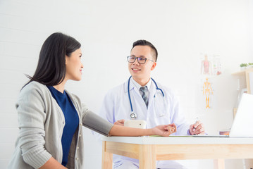 Fototapeta premium Young asian male doctor checking female patient blood pressure at clinic