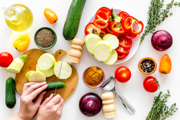 Hands cut different fresh vegetables on cutting board for cooking vegetable stew. White background top view