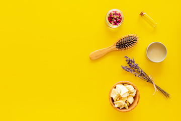 Natural oil for hair. Jojoba, argan, coconut oil near bunch of lavender and hairbrush on yellow background top view copy space