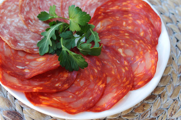 Chorizo and salami sliced and served with parsley on a white plate, close up