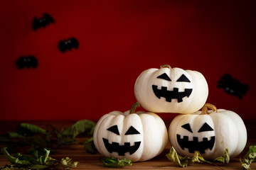 White ghost pumpkin on wooden table with bat on orange background. halloween concept.