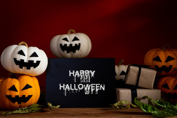 White and yellow ghost pumpkin on wooden table with bat on orange background. halloween concept.