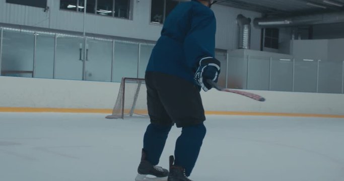 Caucasian male ice hockey player practicing slap shot at the training arena alone, misses the net. 4K UHD 60 FPS
