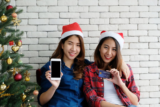 Two young cute asia women holding smartphone with blank screen and credit card for shopping online background,mock up, with happiness, Christmas holiday shopping concept