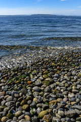 Rocky Puget Sound beach, small rocks, calm sea with small waves, distant island and blue sky with clouds
