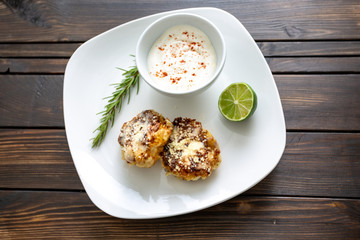Two shrimp cakes on a white plate with a lemon garlic dipping sauces lemon wedge and a stem or rosemary on a wooden table.