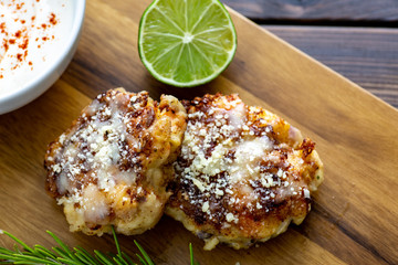 Two shrimp cakes on a cutting board with a lemon garlic dipping sauces lemon wedge and a stem or rosemary on a wooden table.