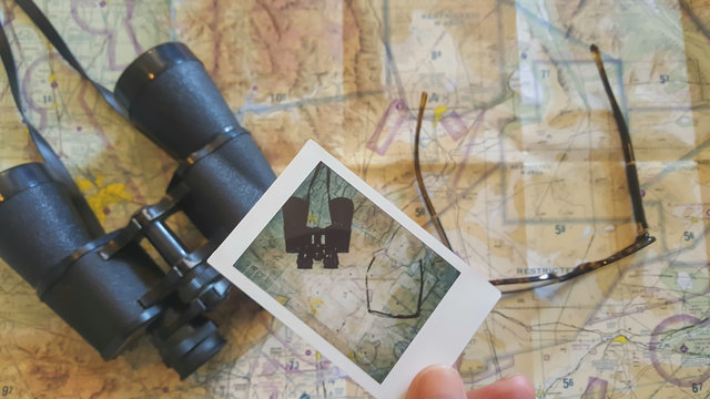 Man holding a polaroid photo over a map with binoculars