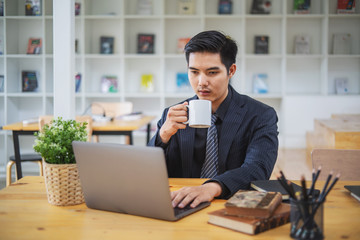 Businessman working on laptop and holding coffee cup while sitting at his working place in office
