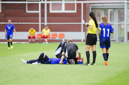 Women football player lying injured on ground, while medic team helping her.