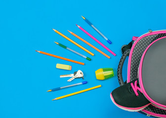 One sneaker sticks out of a school backpack and school supplies on a blue table. Flat lay.