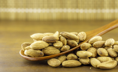 Almonds seeds pour from wood spoon on textured wooden background, top view.