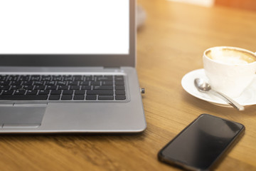 Laptop computer or notebook on wooden table with cup of coffee or hot cappuccino and mobile phone have space on wooden table front view, this image in working and lifestyle concept