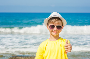 boy in a summer hat by the sea showing thumbs up