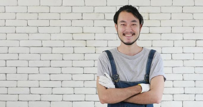 Young good looking Asian technician man in overall stand and smile on the white bricks wall