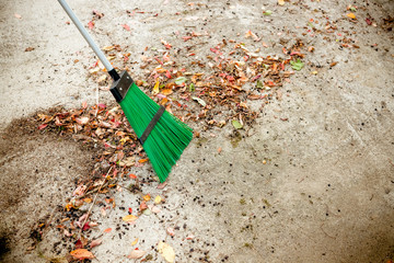 Man sweeps broom leaves in the garden in fall. Colorful dry leaves: red, orange, yellow, green lie in the park on the lawn and paths. Autumn cleaning, work in the garden. Lots of foliage trees, shrubs