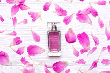 Glass bottle with perfume and petals of a peony flower on a white wooden background.