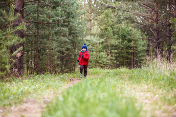cheerful boy in a red jacket running in the forest