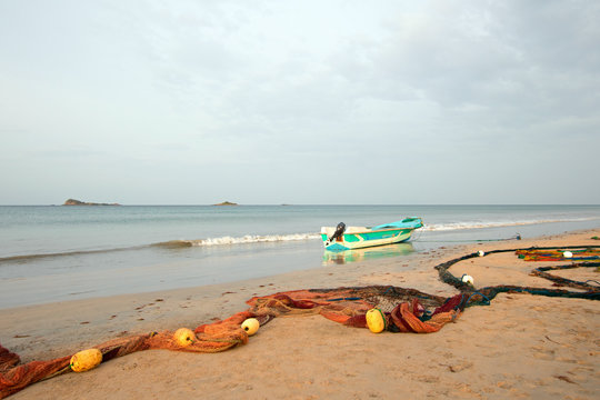 Fishing boat beached next to fishing nets with floats drying on Nilaveli beach in Trincomalee Sri Lanka Asia